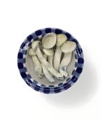 A top view of a blue and white checkered bowl containing several Albino Treasure Coast Premium mushrooms with bluish stems, arranged neatly against a white background.